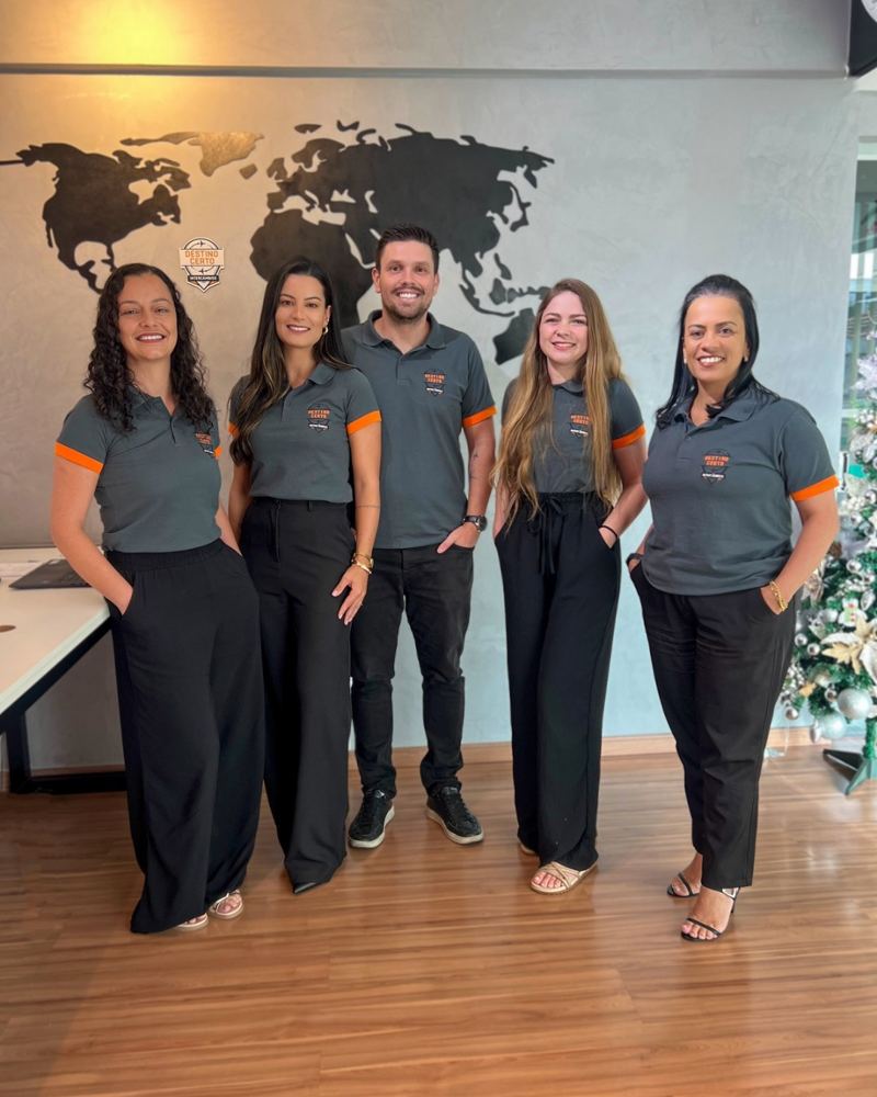 A equipe da Destino Certo Intercâmbios, de camisa da agência, em frente ao mapa-múndi do escritório
