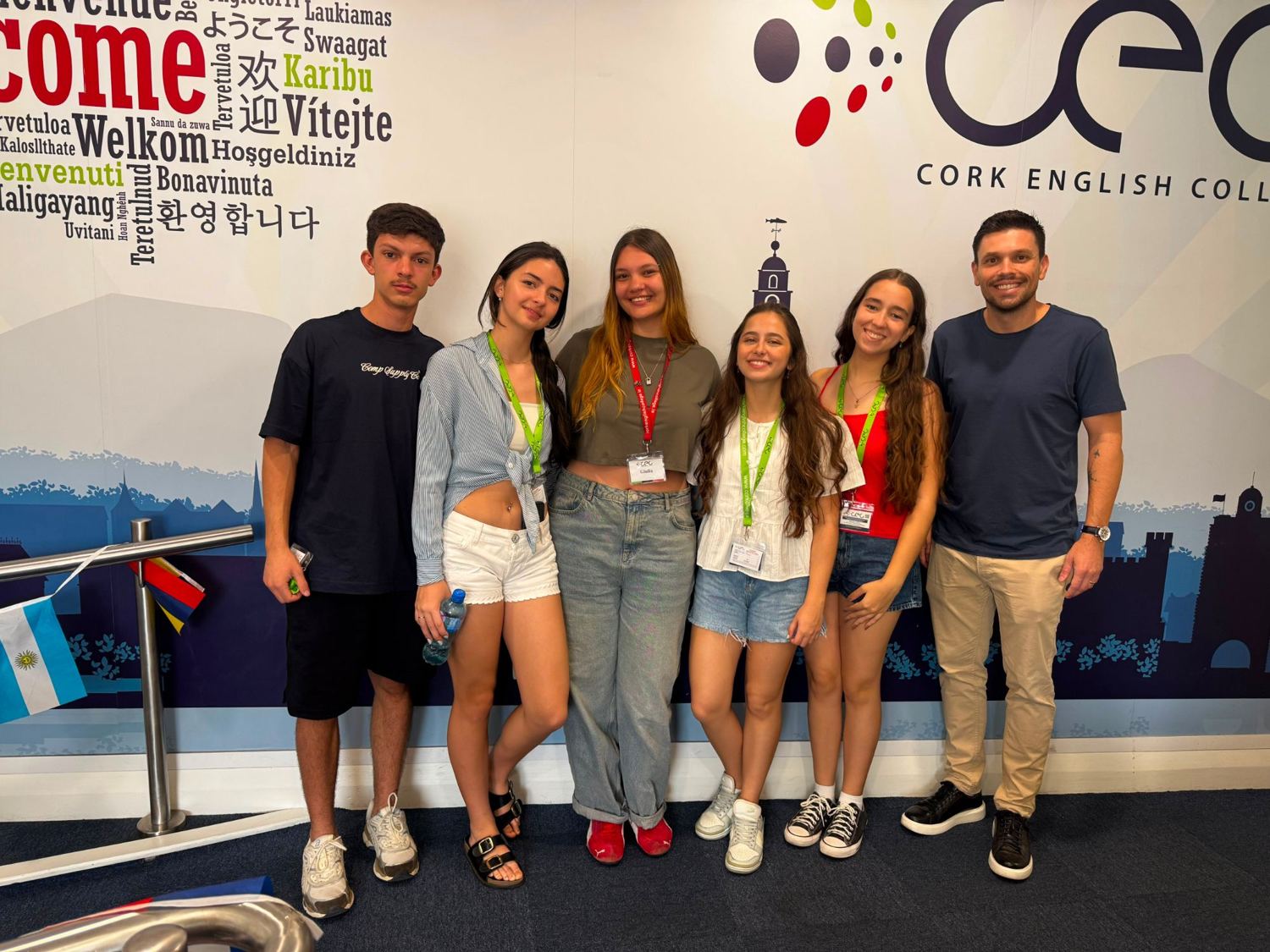 Estudantes e líder em frente à parede de boas-vindas do Cork English College